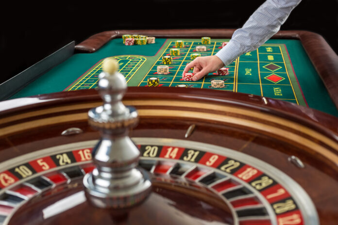 Roulette and piles of gambling chips on a green table.